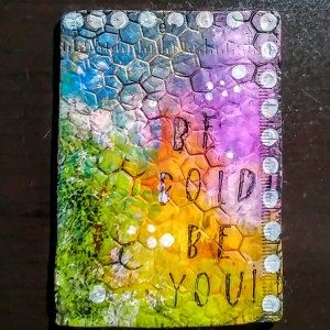 polymer clay written on with a toothpick, rolled onto a honeycomb hot pad multiple directions and stamped with a ruler that has raised numbers and marks. dry brush and fingers to add color in layers and get black to stay down in the grooves and color on top.